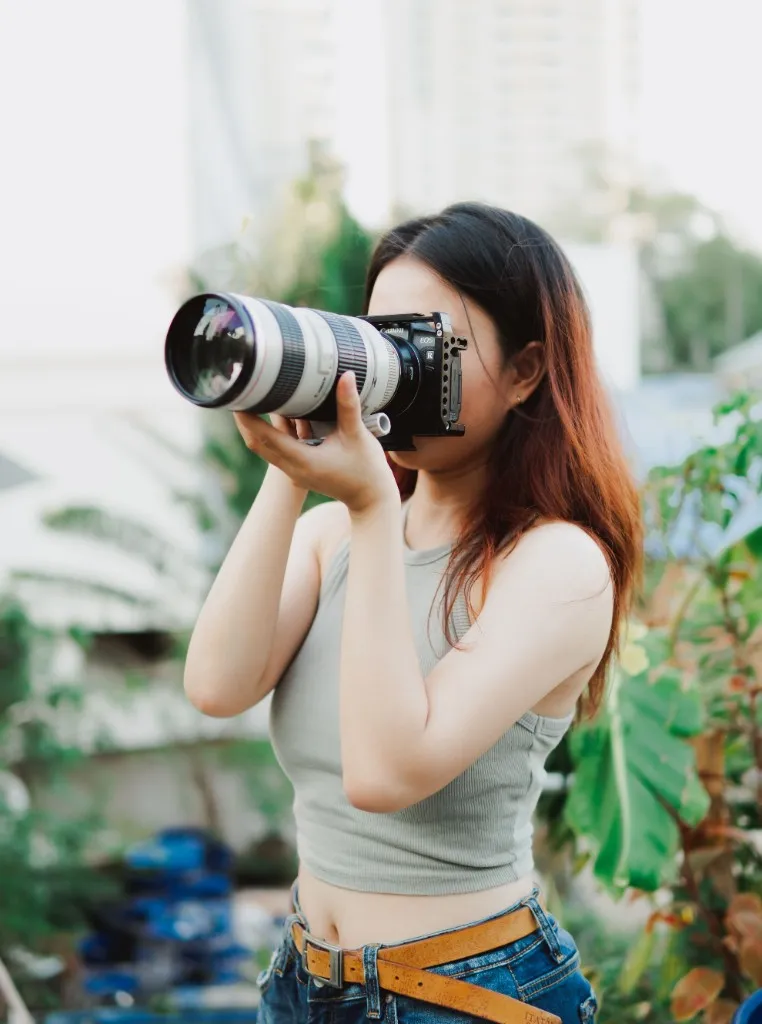 Photographer holding a camera with a long lens up to her face